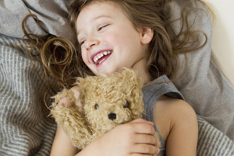 Smiling girl holding teddy bear in bed Photograph by Emely