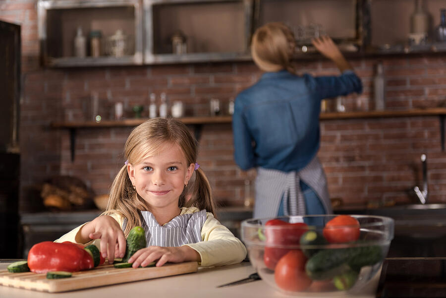 Smiling little girl touching vegetables in the kitchen Photograph by Yacobchuk