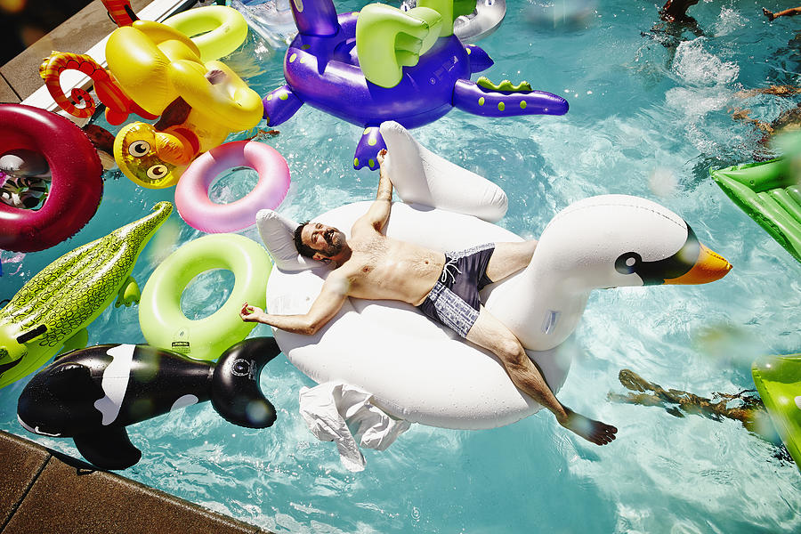 Smiling man relaxing on inflatable swan in pool Photograph by Thomas Barwick