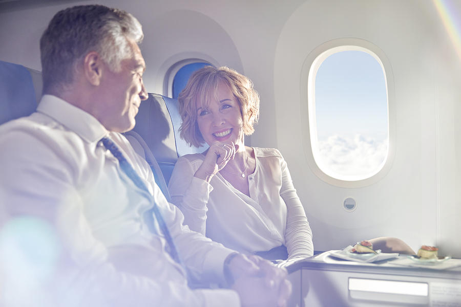 Smiling mature couple eating and talking in first class on airplane Photograph by Caia Image
