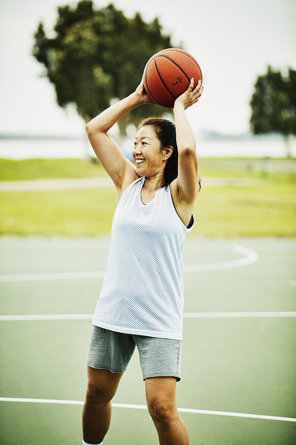 Smiling mature woman looking to make pass during basketball game on outdoor court Photograph by Thomas Barwick