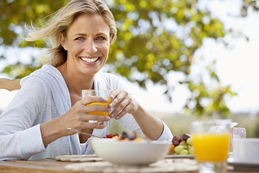 Smiling mature woman with orange juice at breakfast table outdoors Photograph by OJO Images