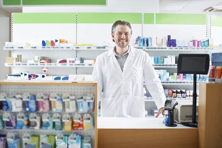 Smiling Pharmacist behind the counter Photograph by Musketeer