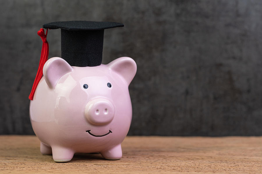 Smiling pink piggy bank wearing graduated hat on wooden table with dark black background and copy space, education fund, Scholarships, university cost and expense or saving for student loan concept Photograph by Nuthawut Somsuk