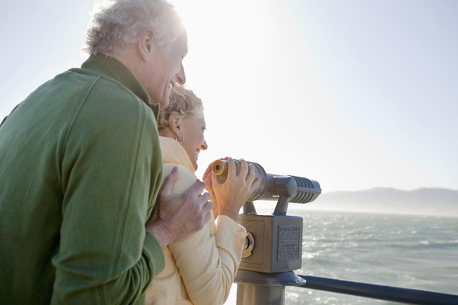 Smiling senior couple looking at ocean with coin-operated binoculars Photograph by Monashee Frantz