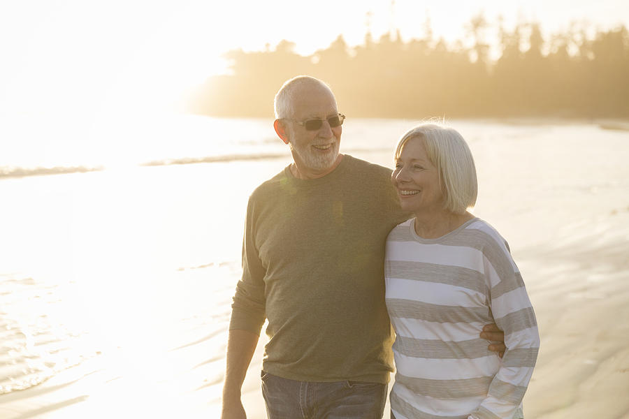 Smiling senior couple walking on beach at sunset Photograph by Compassionate Eye Foundation/Steven Errico