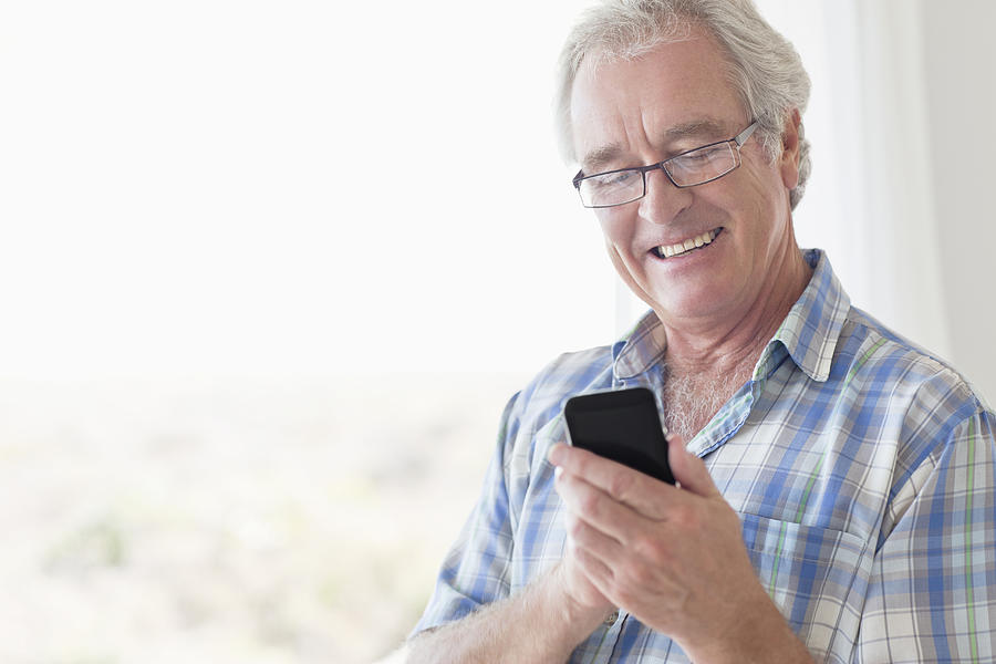 Smiling senior man texting using smart phone Photograph by OJO Images