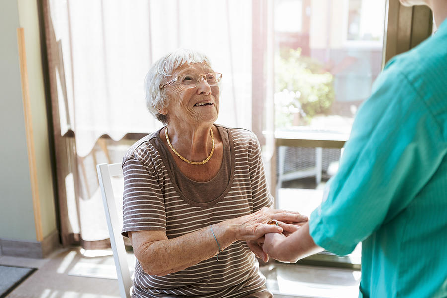 Smiling senior woman holding hands of healthcare worker at nursing home Photograph by Kentaroo Tryman