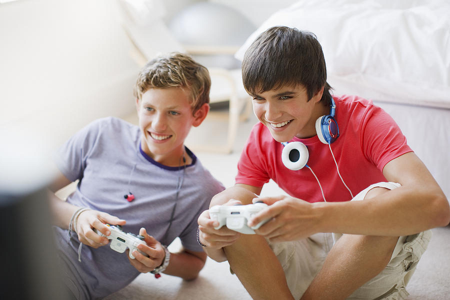 Smiling teenage boys playing video game Photograph by Paul Bradbury