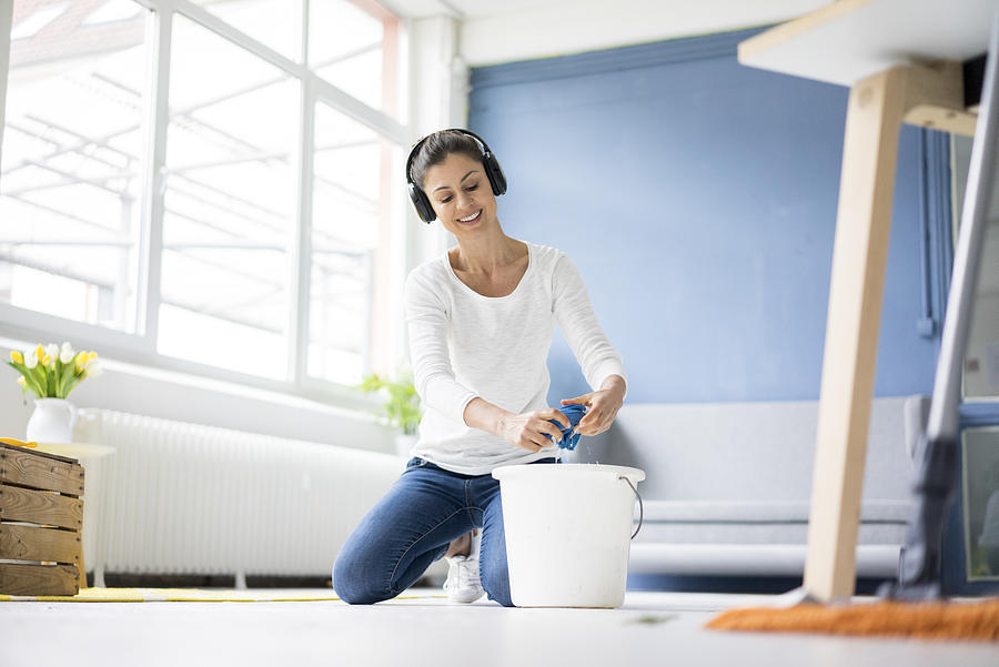 Smiling woman at home wearing headphones wiping the floor Photograph by Westend61