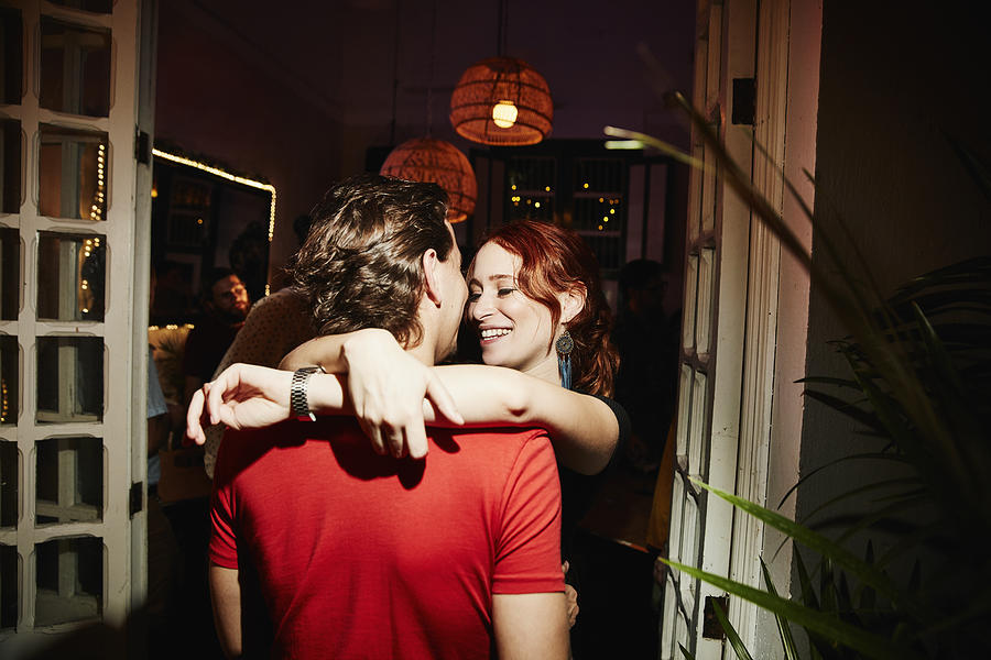 Smiling woman embracing boyfriend during party in night club Photograph by Thomas Barwick