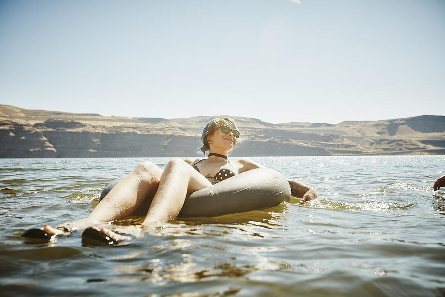 Smiling woman floating in inner tube in river Photograph by Thomas Barwick