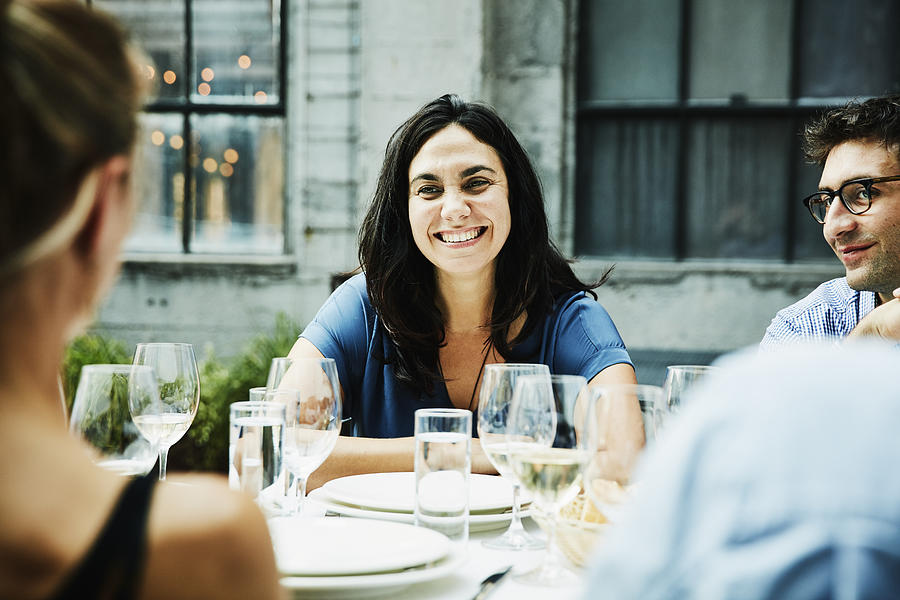 Smiling woman hanging out with friends during dinner on restaurant patio Photograph by Thomas Barwick