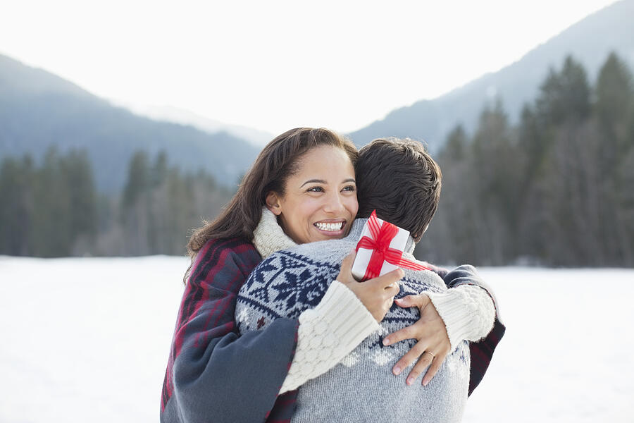 Smiling woman holding Christmas gift and hugging man in snow Photograph by Sam Edwards