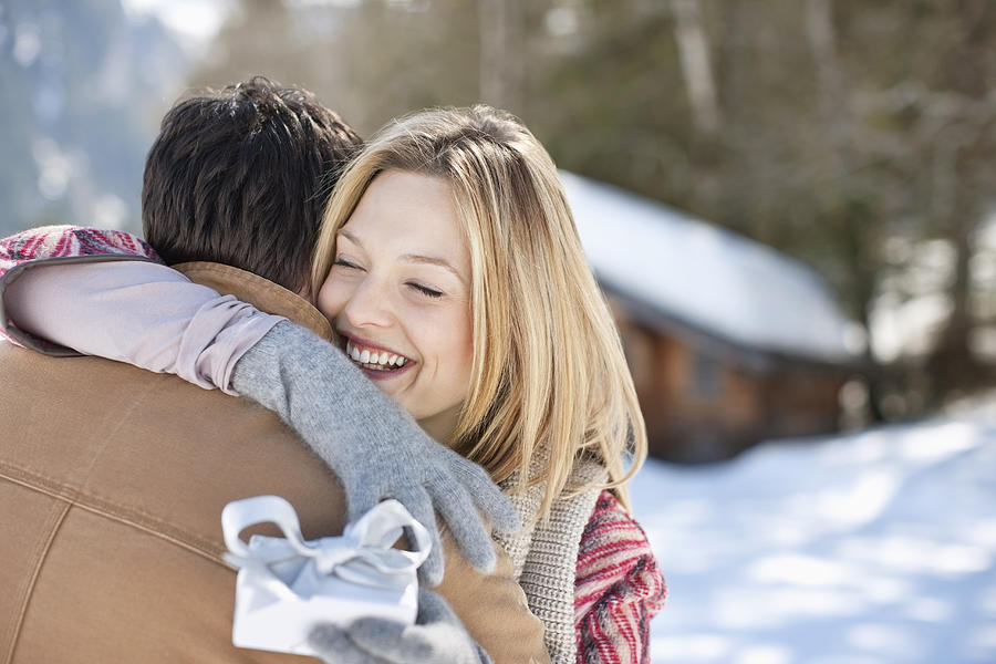 Smiling woman holding Christmas gift and hugging man in snowy field Photograph by Tom Merton