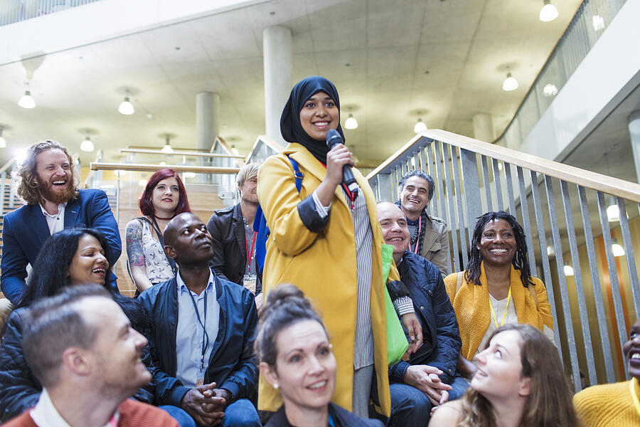 Smiling woman in hijab speaking with microphone in conference audience Photograph by Caia Image