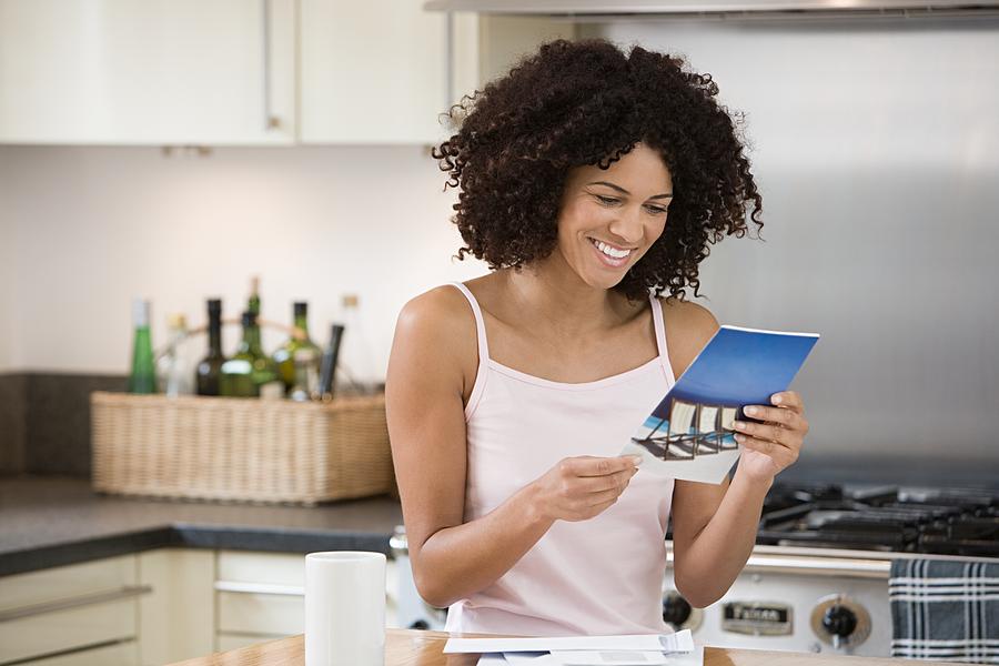 Smiling woman reading a brochure in kitchen Photograph by Image Source