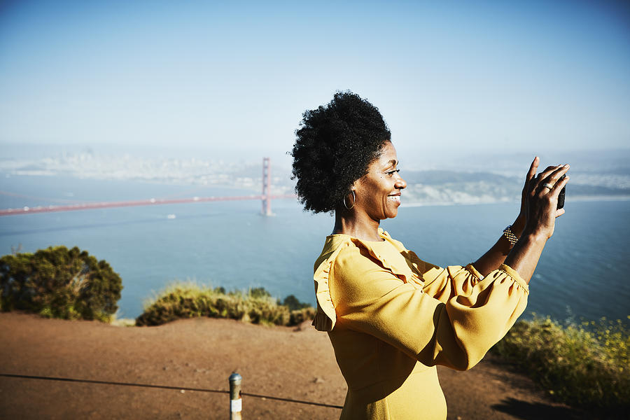 Smiling woman taking photo with smartphone while standing at vista above San Francisco Photograph by Thomas Barwick