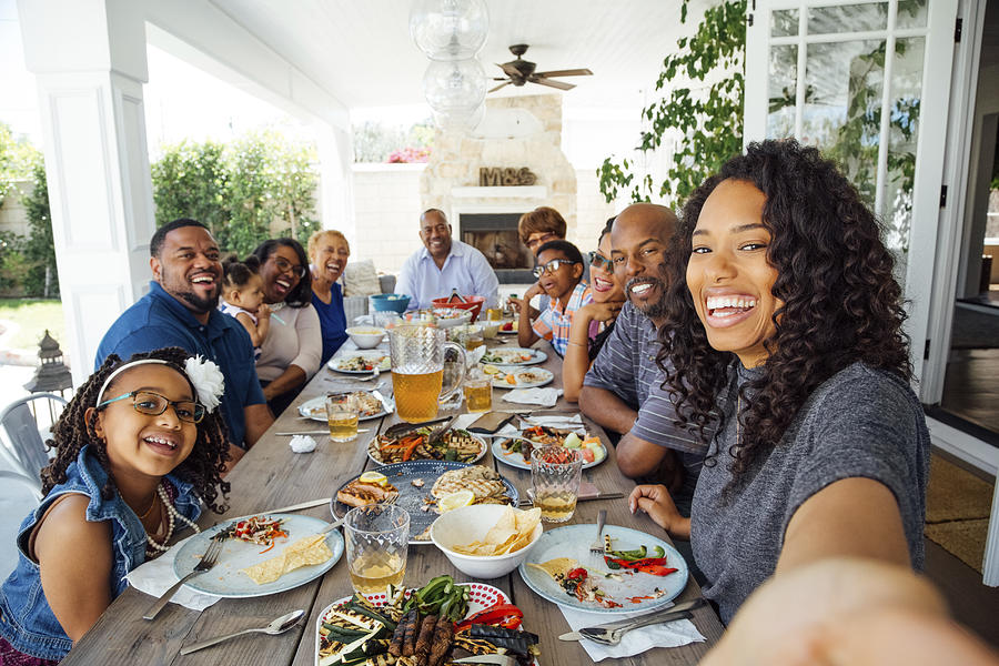 Smiling woman taking selfie with family at dinner party Photograph by The Good Brigade