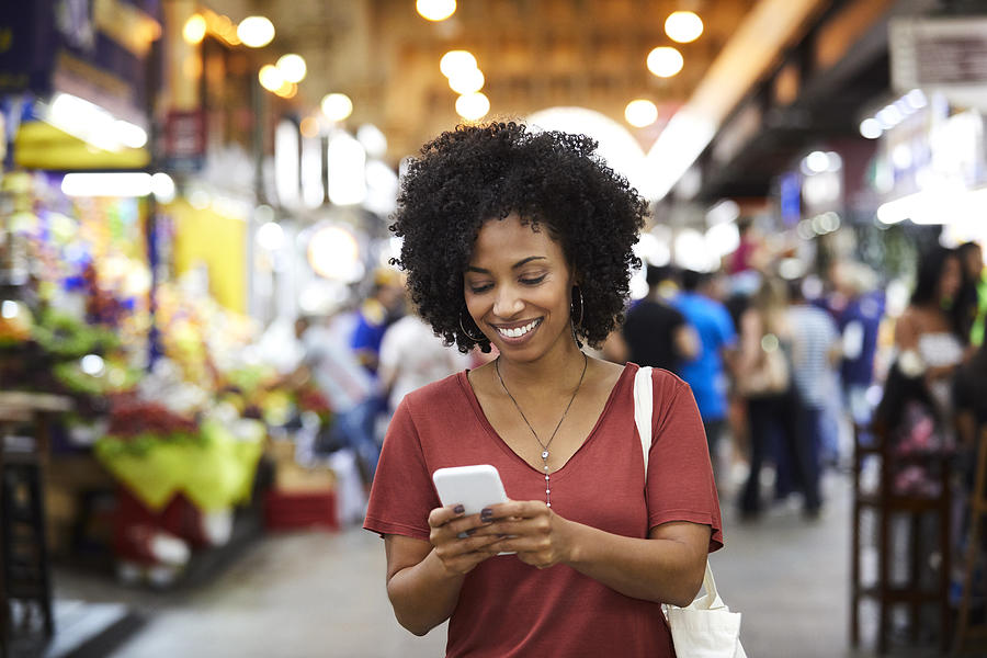 Smiling woman using smart phone at supermarket Photograph by Morsa Images