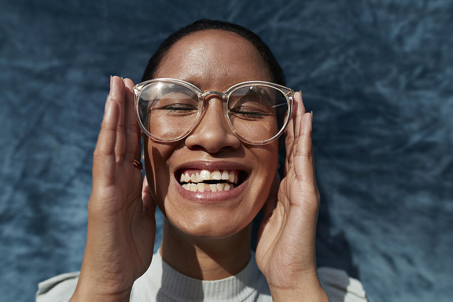 Smiling woman wearing eyeglasses against blue wall Photograph by Klaus Vedfelt