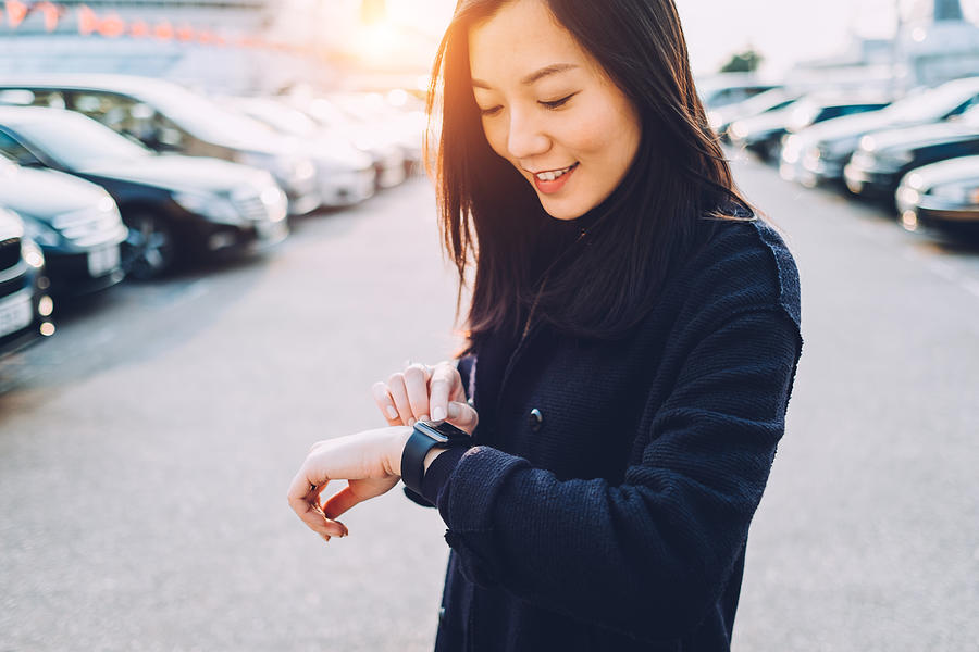 Smiling young Asian girl checking her smart watch in city street Photograph by D3sign