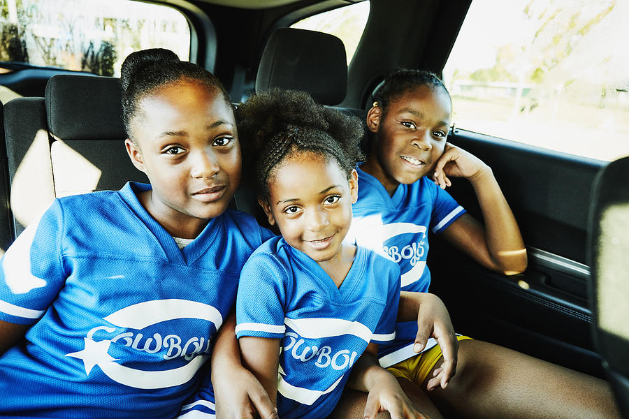 Smiling young cheerleaders sitting in back seat of car on the way to practice Photograph by Thomas Barwick
