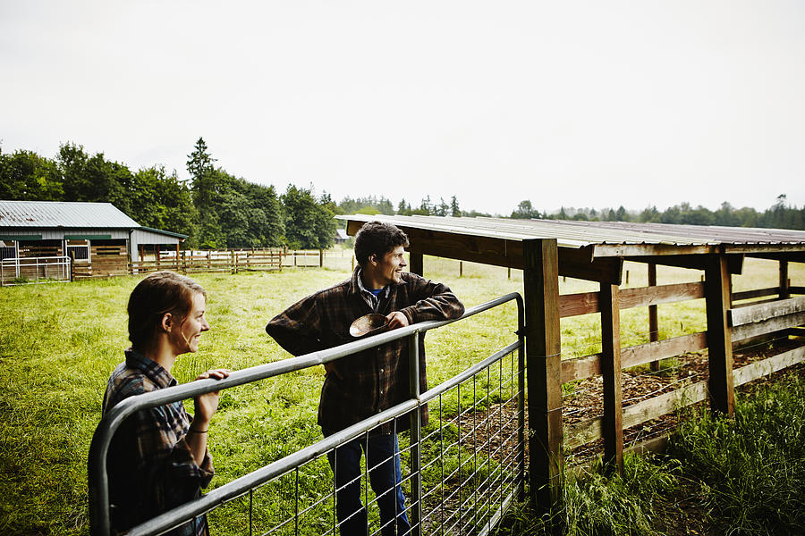 Smiling young farmers looking out at pasture Photograph by Thomas Barwick