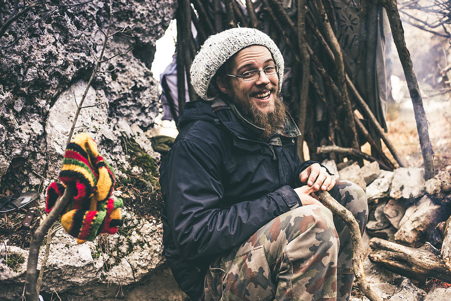 Smiling Young Man with Dreadlocks Sitting By a Fireplace in Nature Photograph by CasarsaGuru