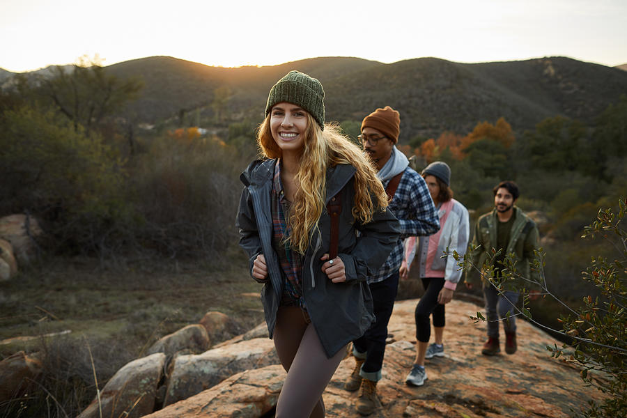 Smiling young woman and friends hiking up a hill together Photograph by Goodboy Picture Company
