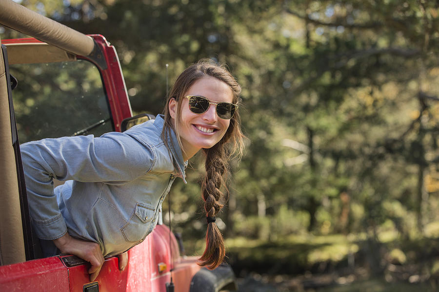 Smiling young woman leaning out of jeep Photograph by Morsa Images