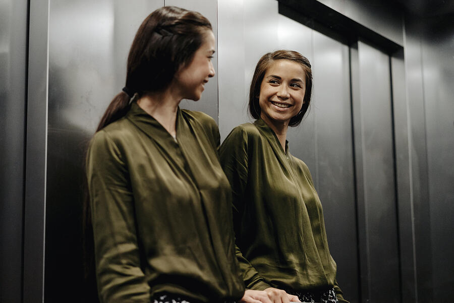 Smiling young woman looking in mirror in elevator Photograph by Westend61