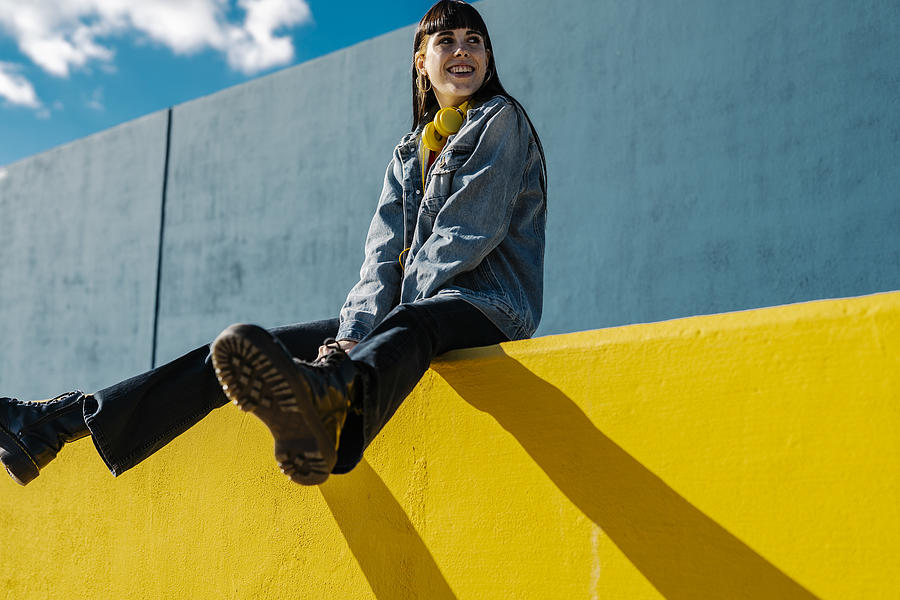 Smiling young woman sitting on a yellow wall in sunny day Photograph by Coroimage