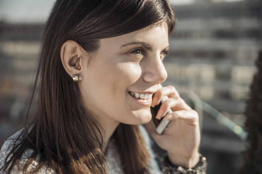Smiling young woman with hearing aid on the phone Photograph by Westend61