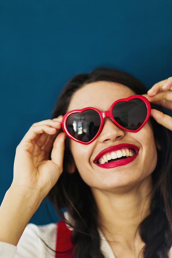Smiling young woman with red heart shaped sunglasses Photograph by Les Hirondelles Photography