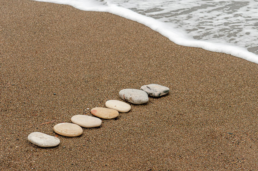 Smooth beach stones in a raw on a sandy coastline and foam of sea water. Photograph by Michalakis Ppalis