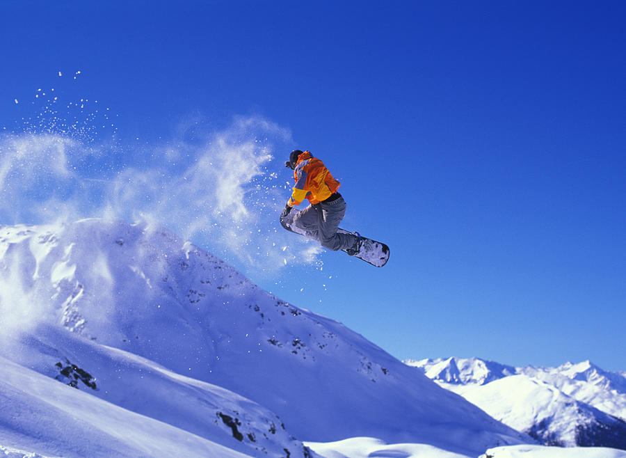 Snowboarder in mid-jump with a cloud of snow trailing behind Photograph by Creativaimage