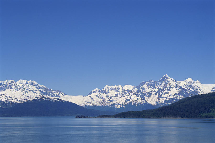 Snowy mountain range over lake Photograph by Comstock