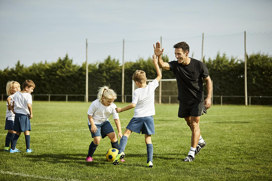 Soccer coach high-fiving with boy during practice Photograph by Morsa Images