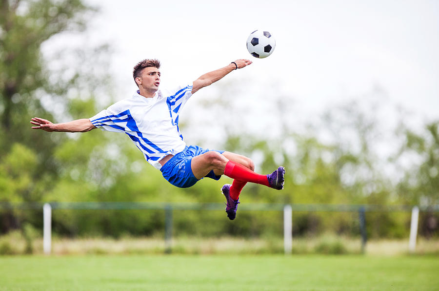 Soccer player kicking the ball while being in mid air. Photograph by Skynesher