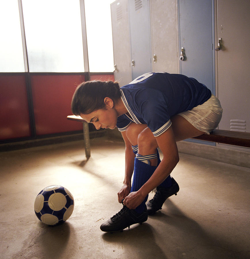 Soccer player tying cleats in locker room Photograph by Pnc