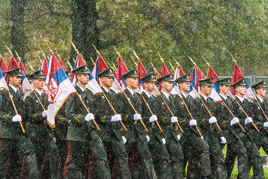 Soldiers marching on a military parade carrying flags in downpour. Photograph by Zoran Kolundzija