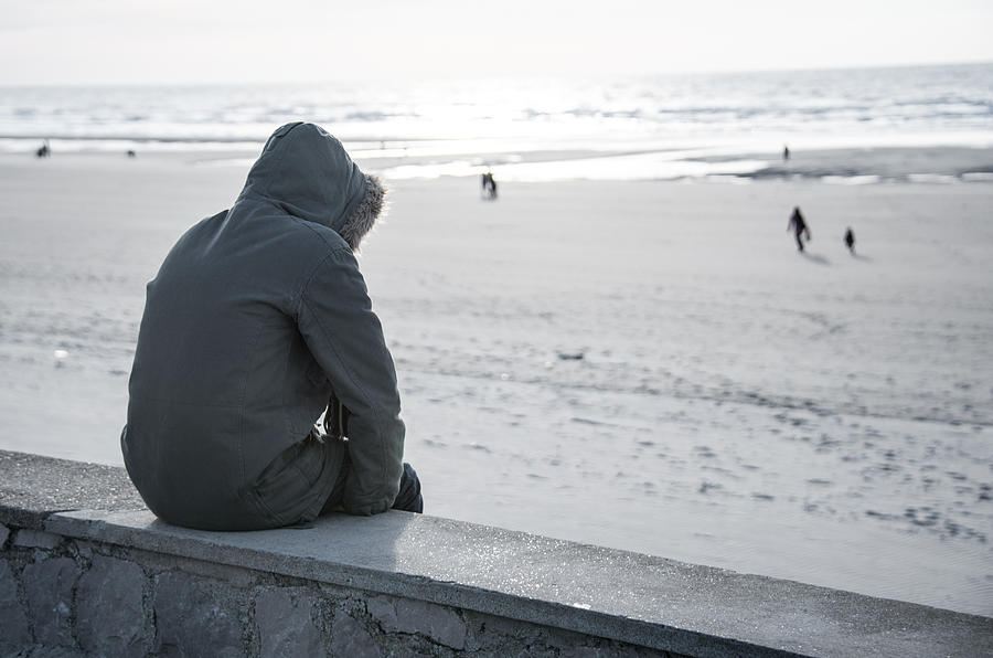 Solitary person in hooded parka coat sits on sea wall alone Photograph by ImageGap