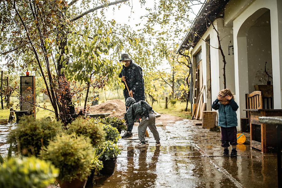 Son helping father and sweeping water from front yard on rainy day Photograph by Freemixer