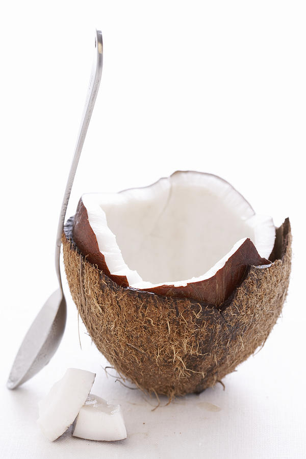 Spoon leaning on split coconut, close-up Photograph by Martin Poole