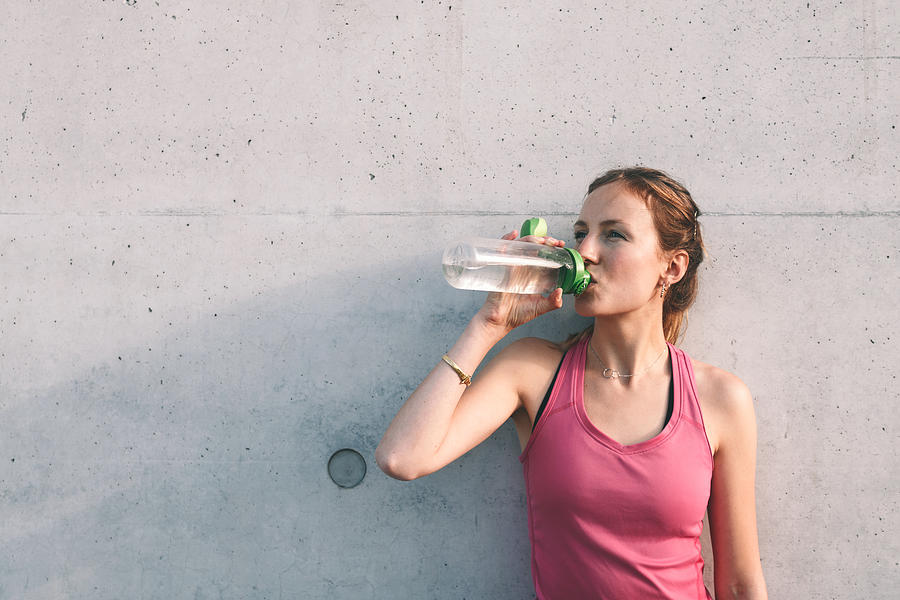 Sportswoman Drinking Water In Front Of Concrete Wall Photograph by Golero
