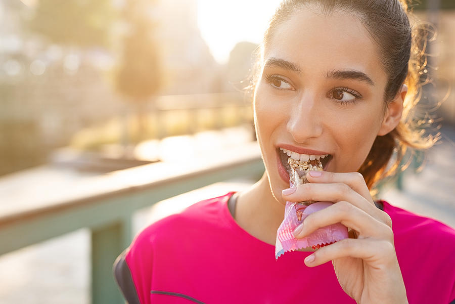 Sporty woman eating energy bar Photograph by Ridofranz