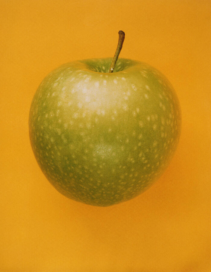 Spotted Green Apple On Orange Background Photograph by Abrams/Lacagnina
