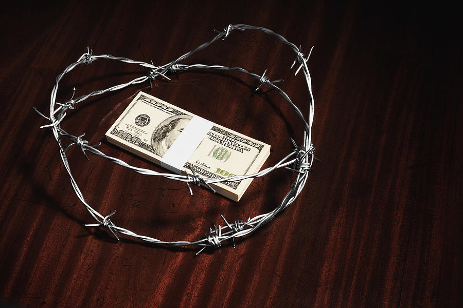 Stack of hundred dollar bills surrounded by barbed wire Photograph by Microzoa Limited