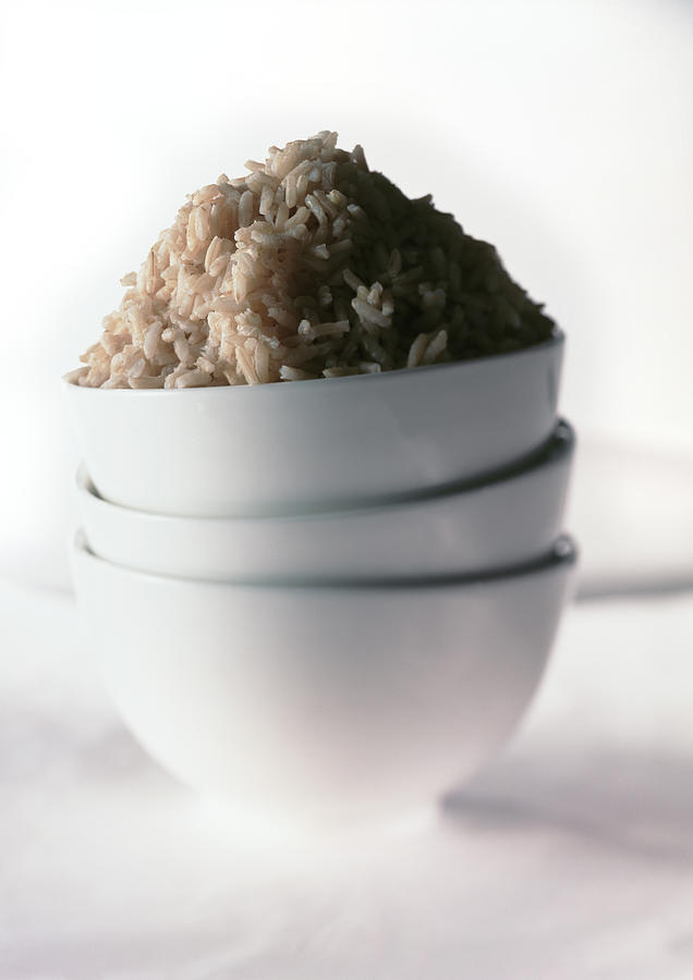 Stack of three white bowls, mound of brown rice in top bowl, close-up Photograph by Isabelle Rozenbaum & Frederic Cirou